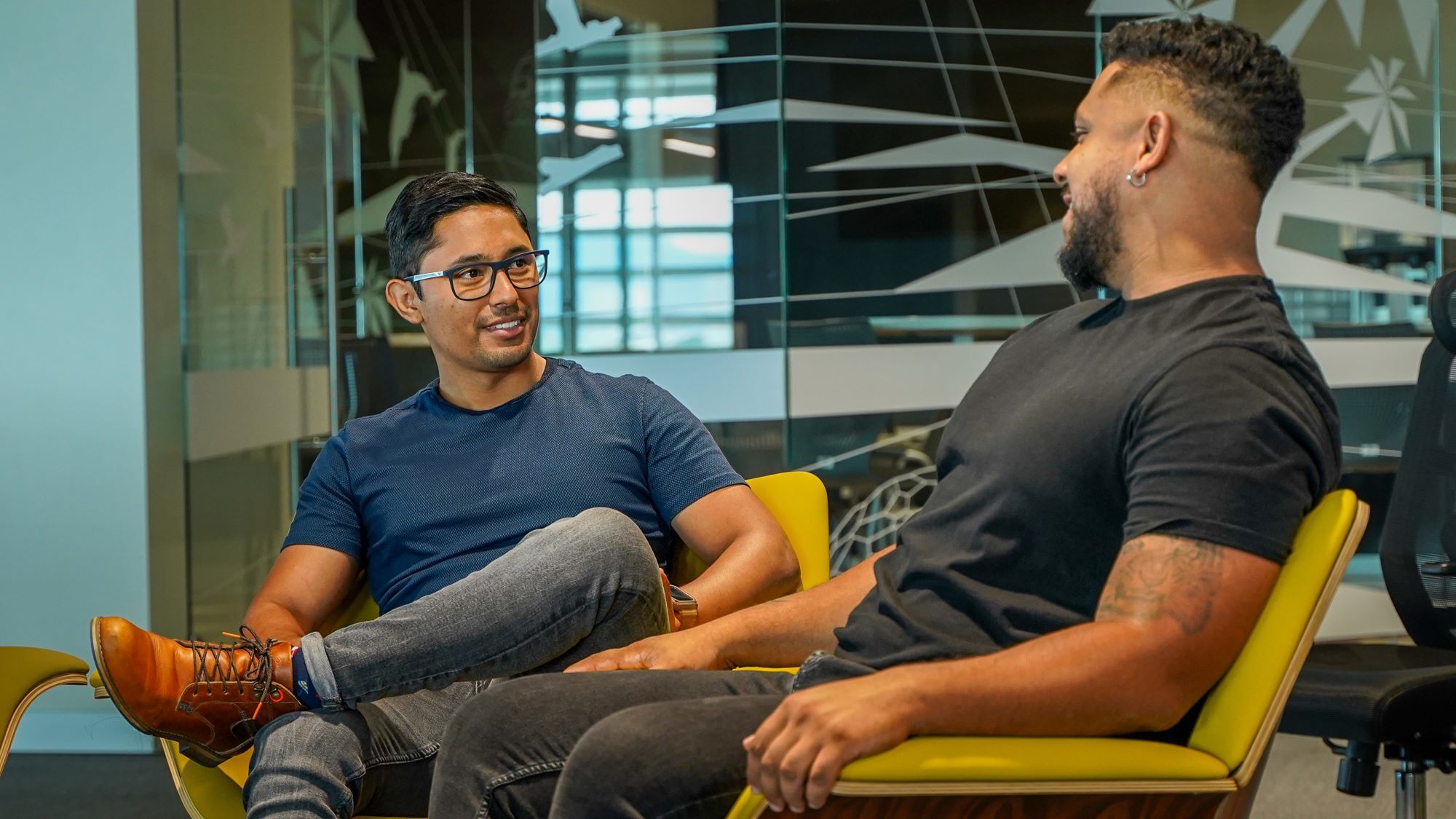 An image of two men seated in chairs talking in an office setting.