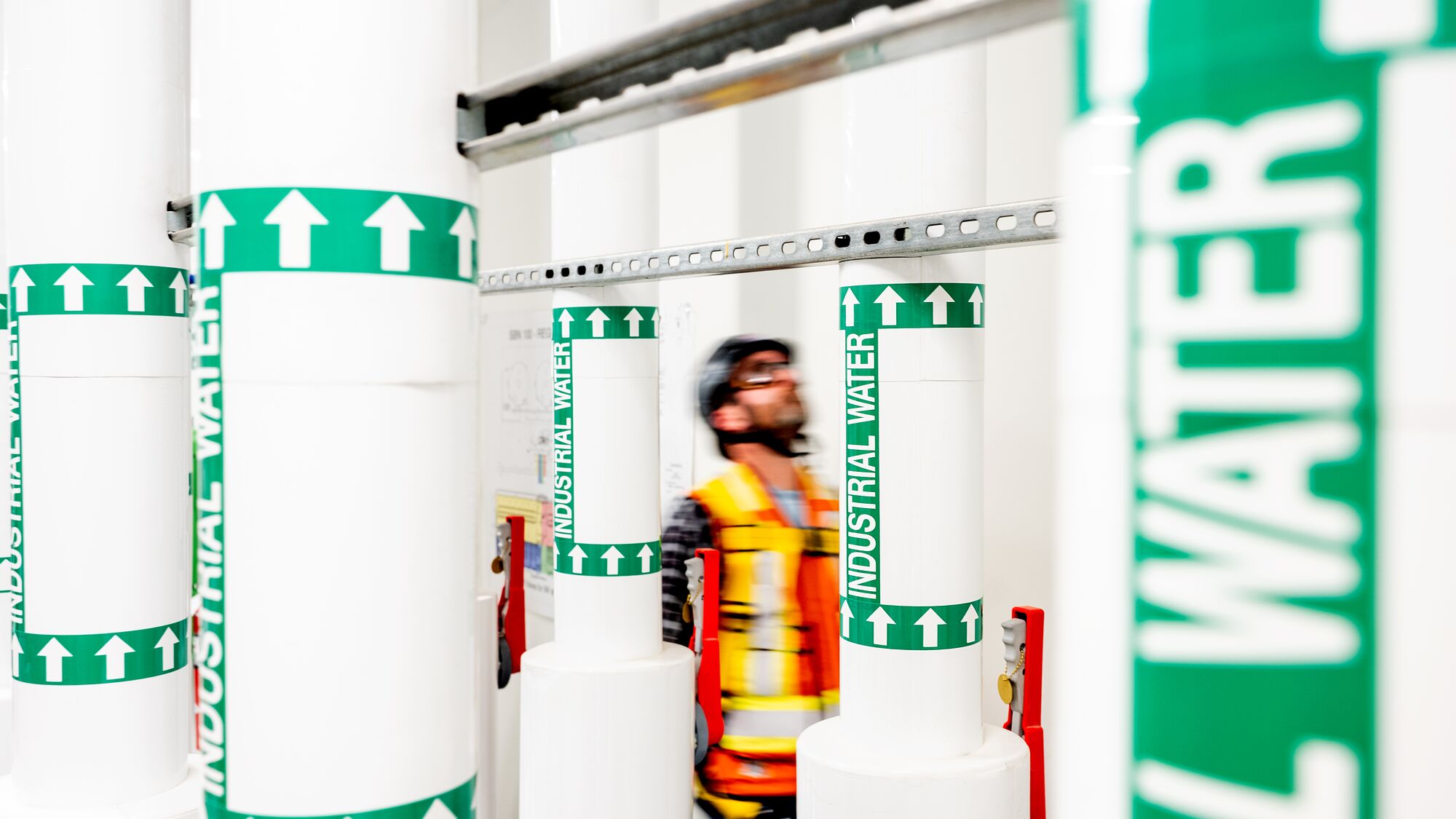 Worker in safety vest amid industrial water pipe labels