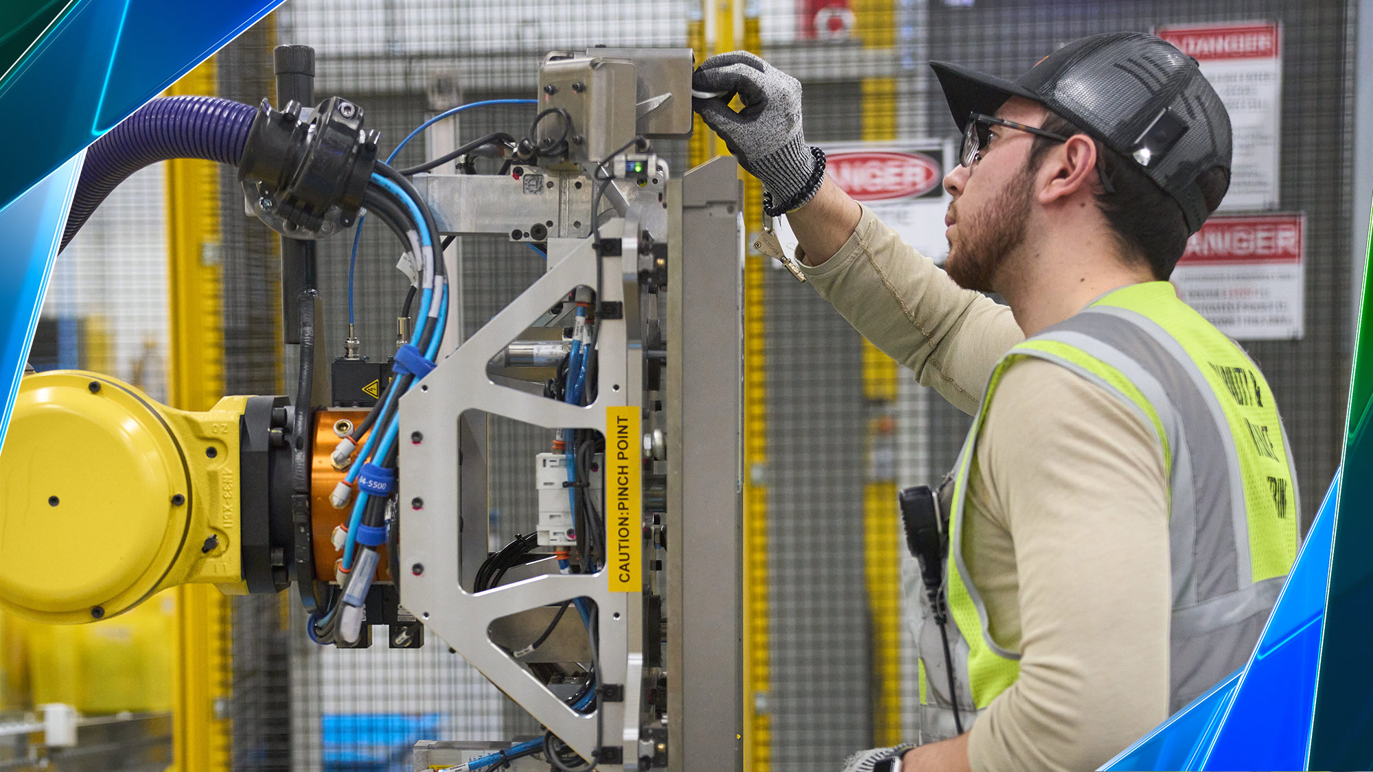 An Amazon employee wears a yellow safety vest and works on a robot.