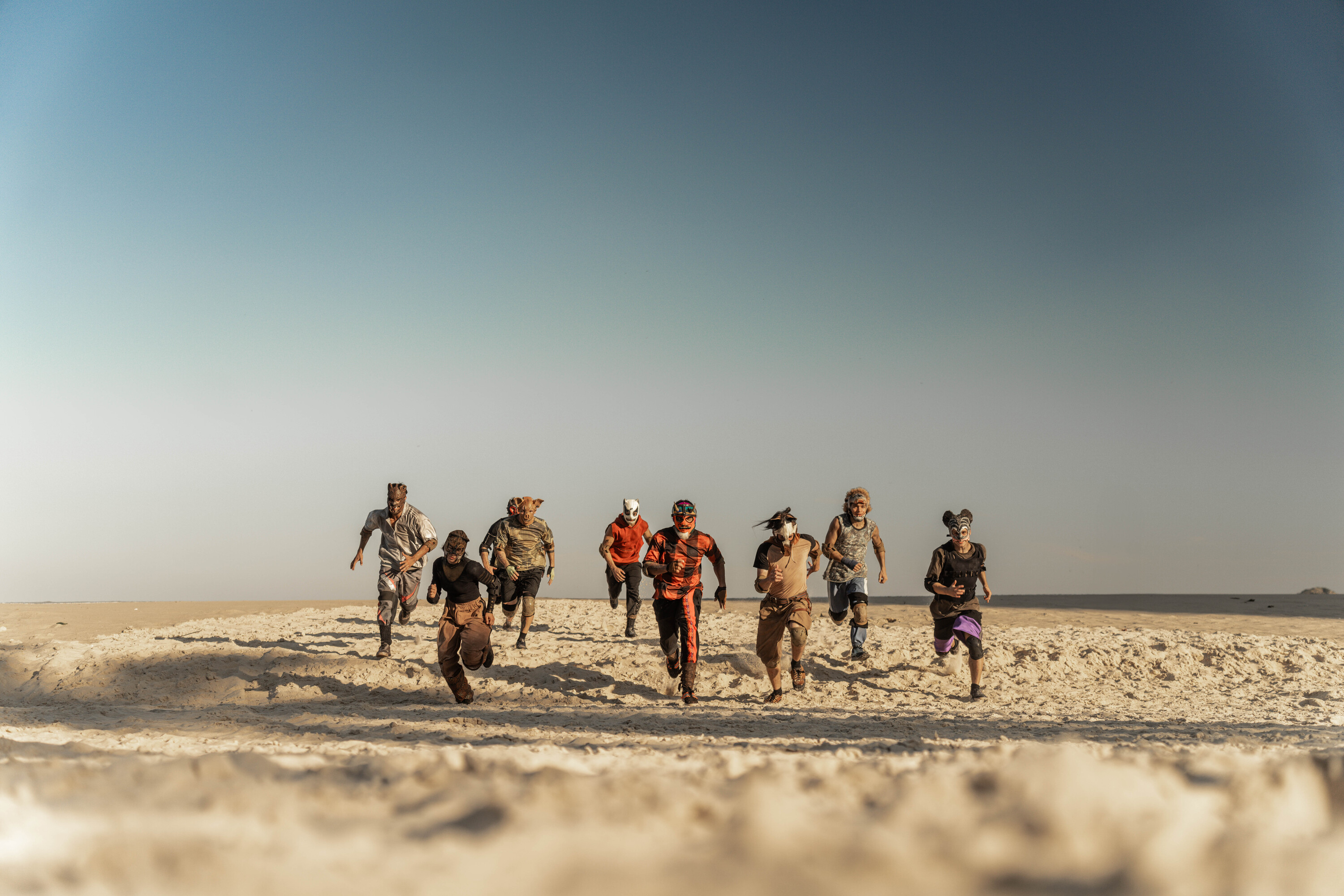 Competidores mascarados correm por uma praia em Corrida dos Bichos