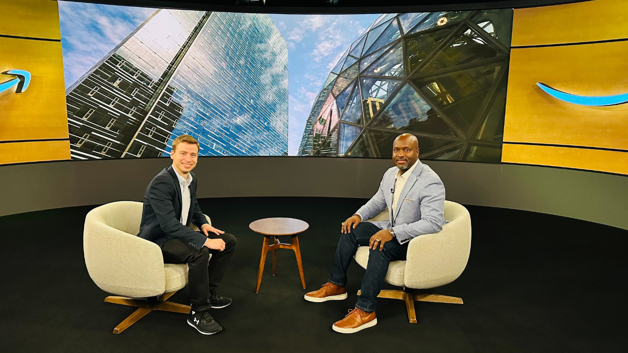 Two men smile for a photo sitting across from one another in an interview setup.