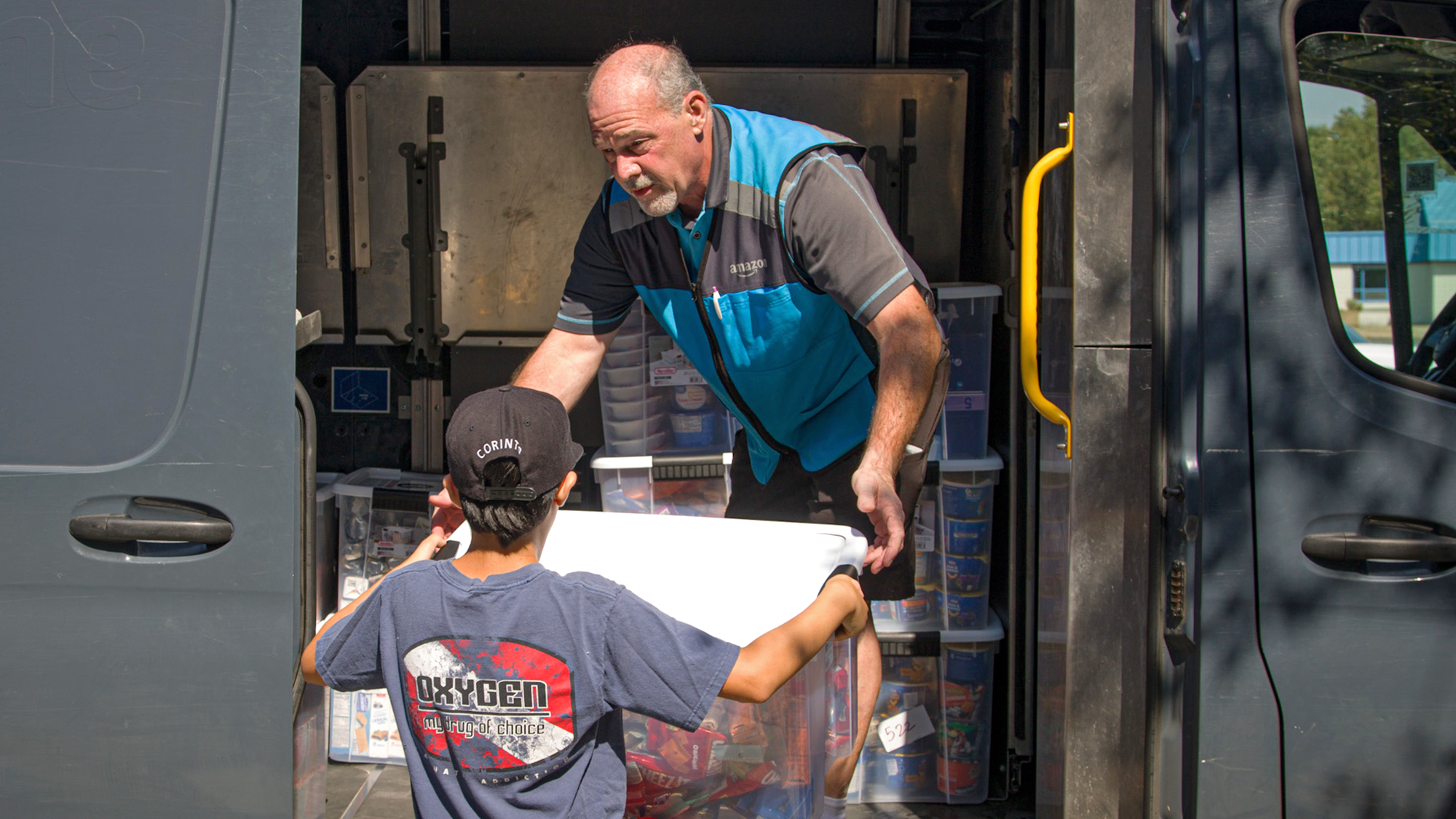 A volunteer handing a bin of donated items to an Amazon delivery driver in a delivery van.