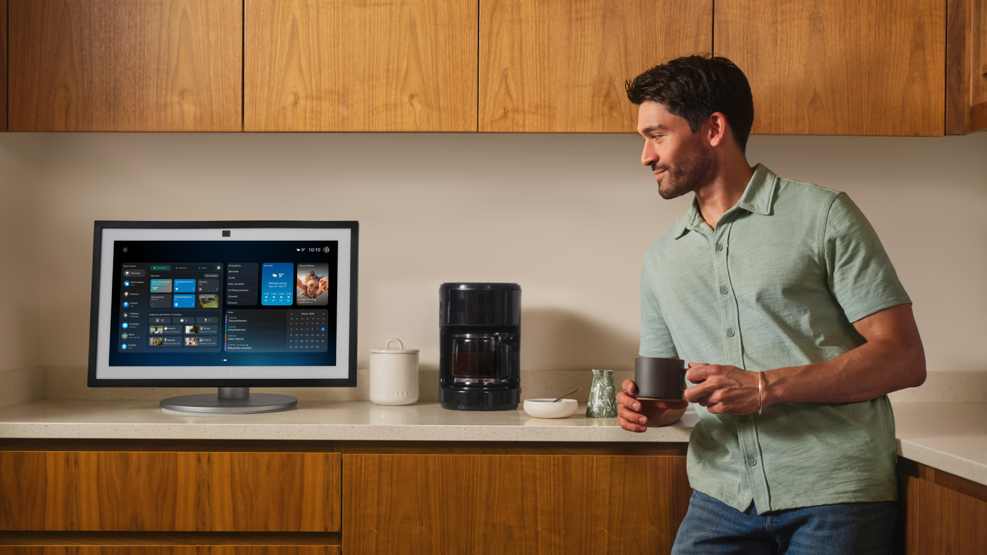 A man holding a coffee in a green shirt staring at his Alexa+ screen in German.